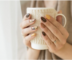 mani con nail art sui colori del marrone ed ocra che impugnano una tazza bianca 